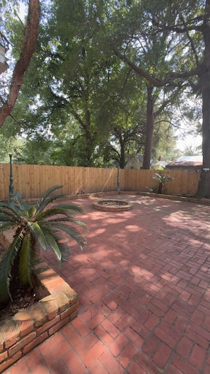A brick patio with a wooden fence and trees. - Camellia Key - Cozy 2BR Home with Fenced Backyard (Alexandria)