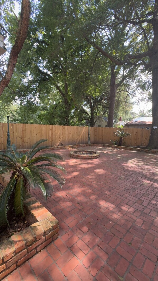 A brick patio with a wooden fence and trees.