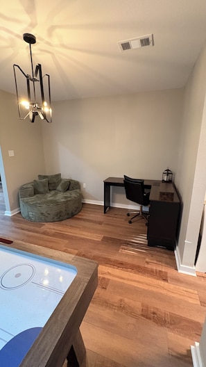 A room with a wooden floor, a desk, a bean bag, and a ceiling light fixture. - Camellia Key - Cozy 2BR Home with Fenced Backyard (Alexandria)