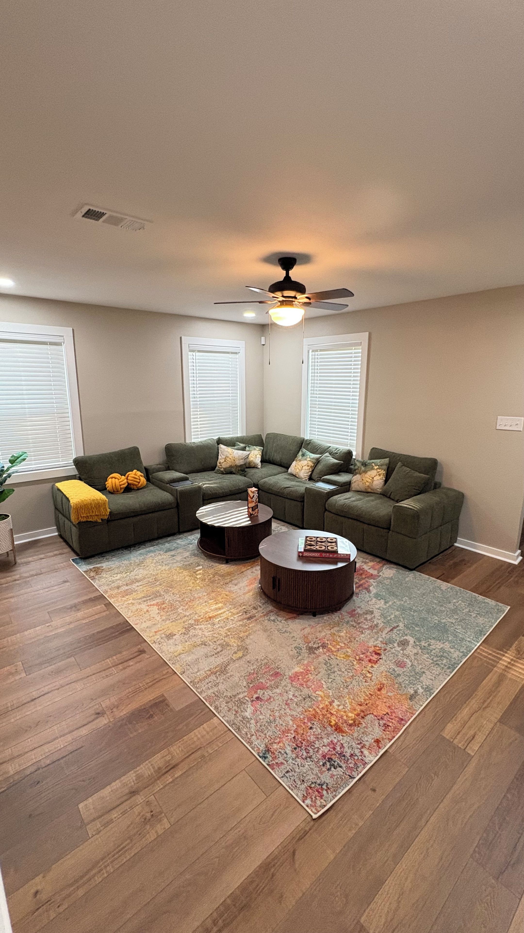 A living room with a sectional sofa, two coffee tables, a ceiling fan, and a patterned rug.