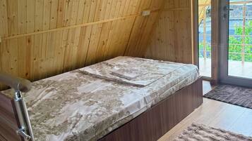 A small, wooden room with a single bed, a wooden staircase, and a view through a glass door.