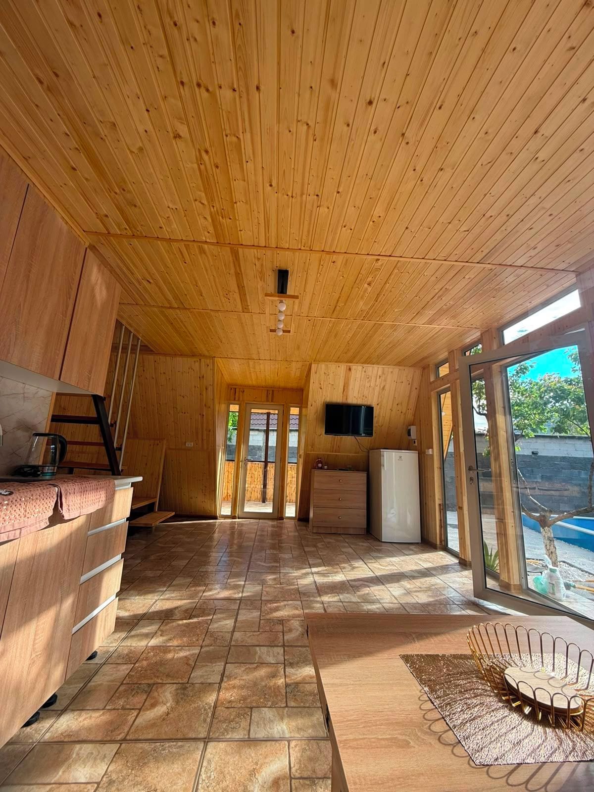 A wooden interior with a kitchen area, a dining table, and a seating area with a decorative chair.