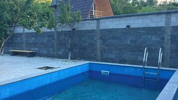A rectangular swimming pool with a ladder on one side, surrounded by a stone wall and a wooden deck.