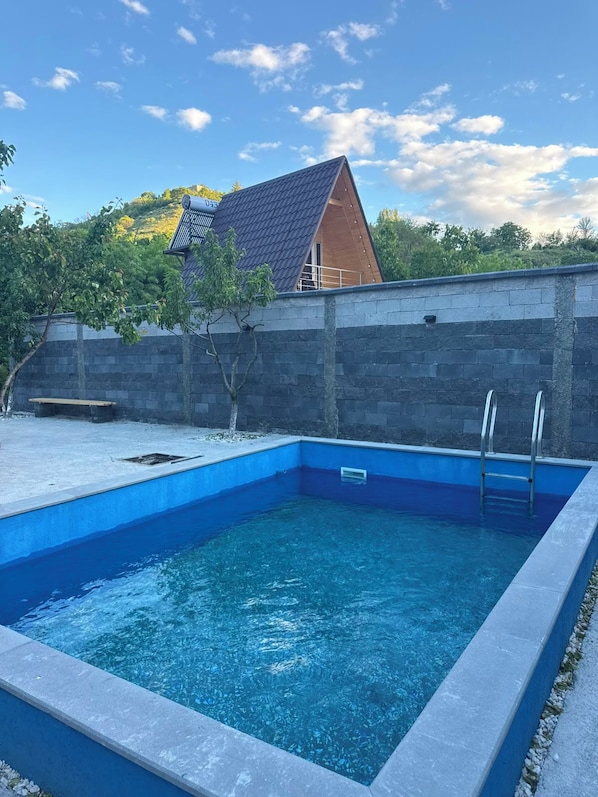 A rectangular swimming pool with a ladder on one side, surrounded by a stone wall and a wooden deck.