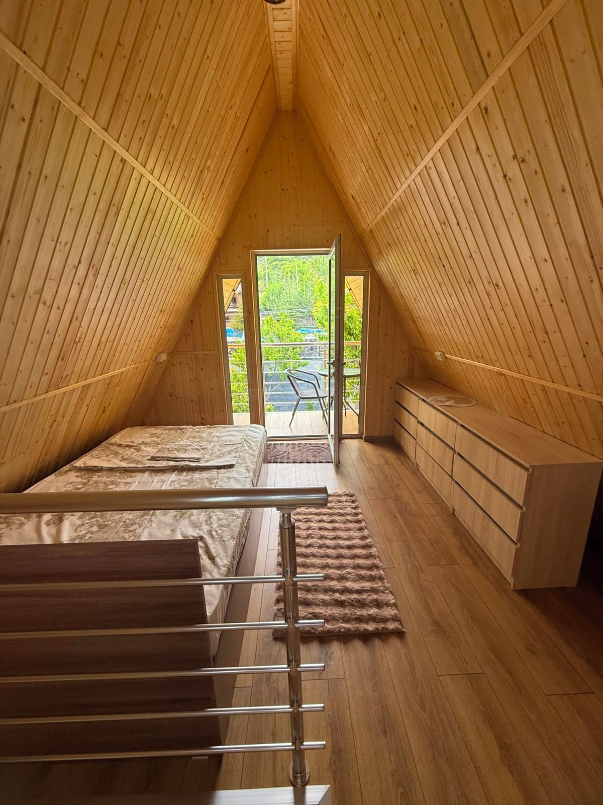 A wooden attic bedroom with a bed, a bench, and a view of greenery outside.