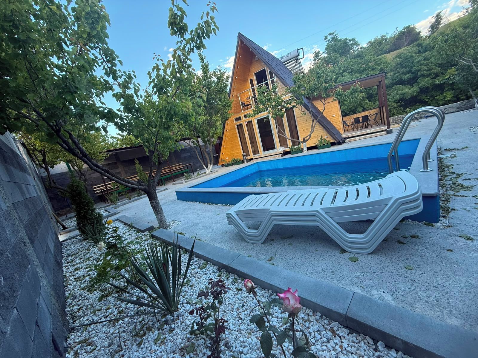 A modern building with a pool, surrounded by a gravel area with a lounge chair and a small garden.