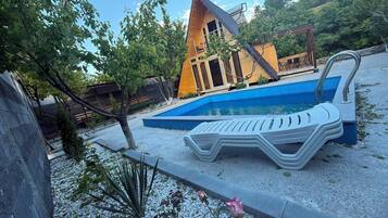 A modern building with a pool, surrounded by a gravel area with a lounge chair and a small garden.