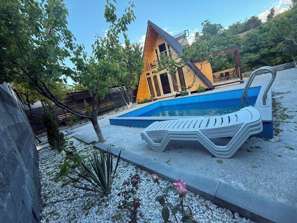 A modern building with a pool, surrounded by a gravel area with a lounge chair and a small garden.