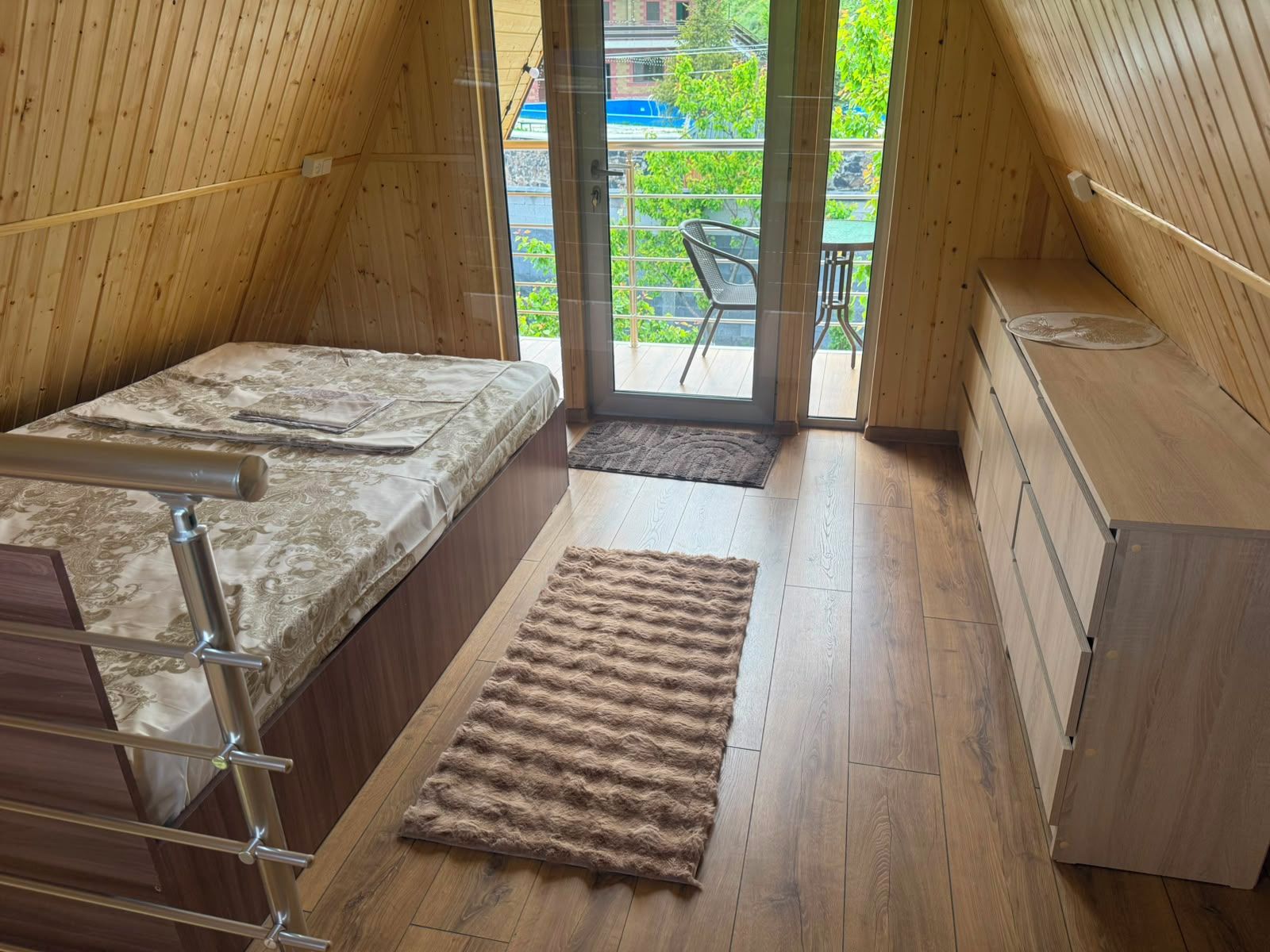 A compact bedroom with a bed, a small desk, and a view through a glass door.