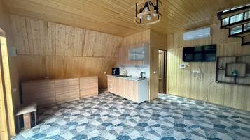 Een kamer met een schuine plafond, een ingebouwde keuken, een vloer met een stenen patroon en een aan de muur bevestigde televisie.