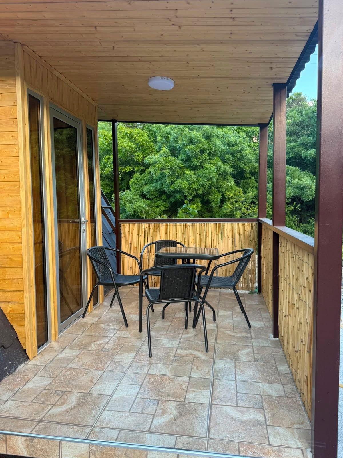 Un porche cubierto con una mesa y sillas, una puerta corrediza de vidrio y vistas a un bosque.