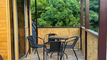 Un porche cubierto con una mesa y sillas, una puerta corrediza de vidrio y vistas a un bosque.