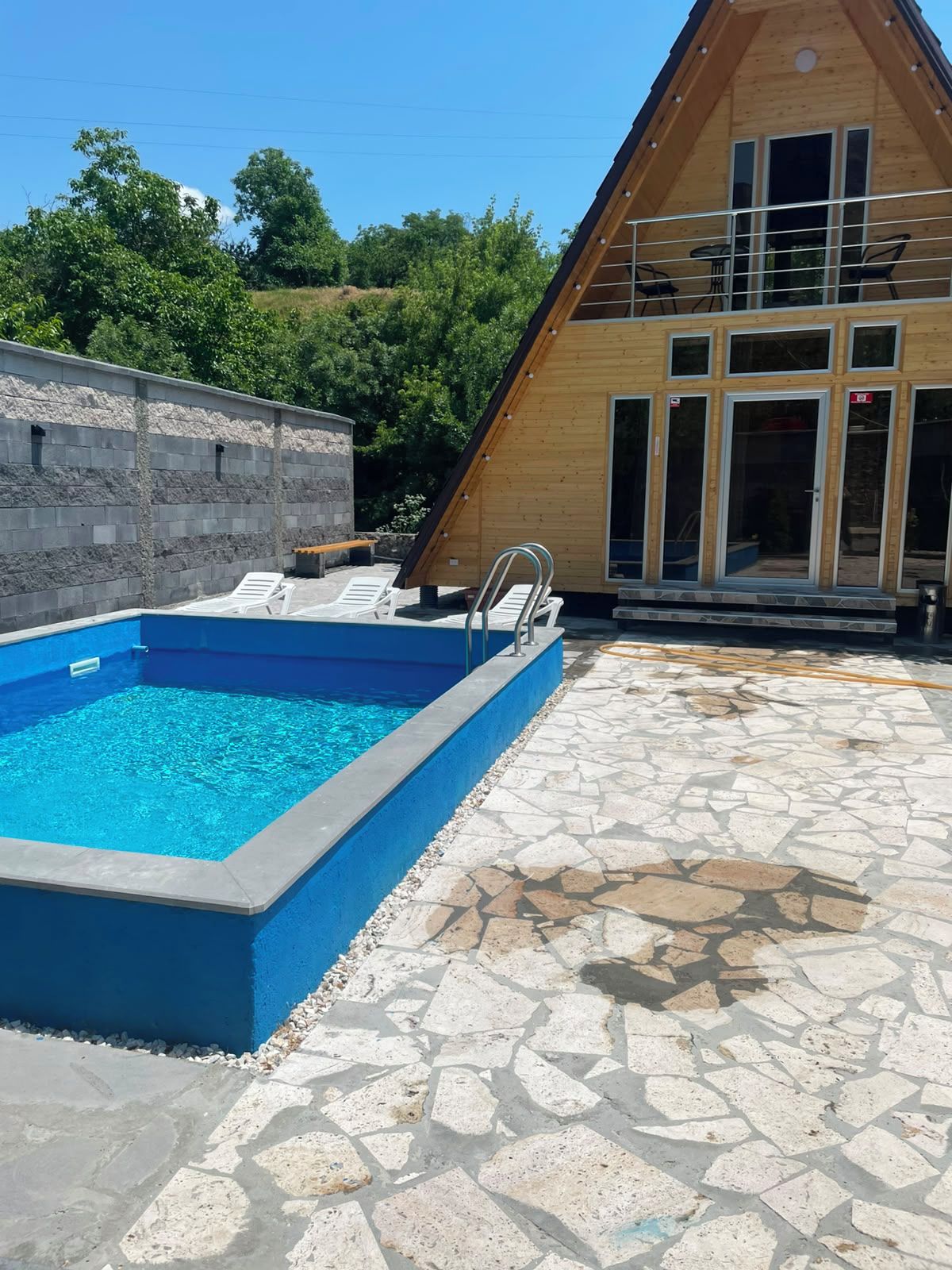 A swimming pool with a stone deck, a wooden building with large windows, and a stone wall.