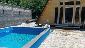 A swimming pool with a stone deck, a wooden building with large windows, and a stone wall.