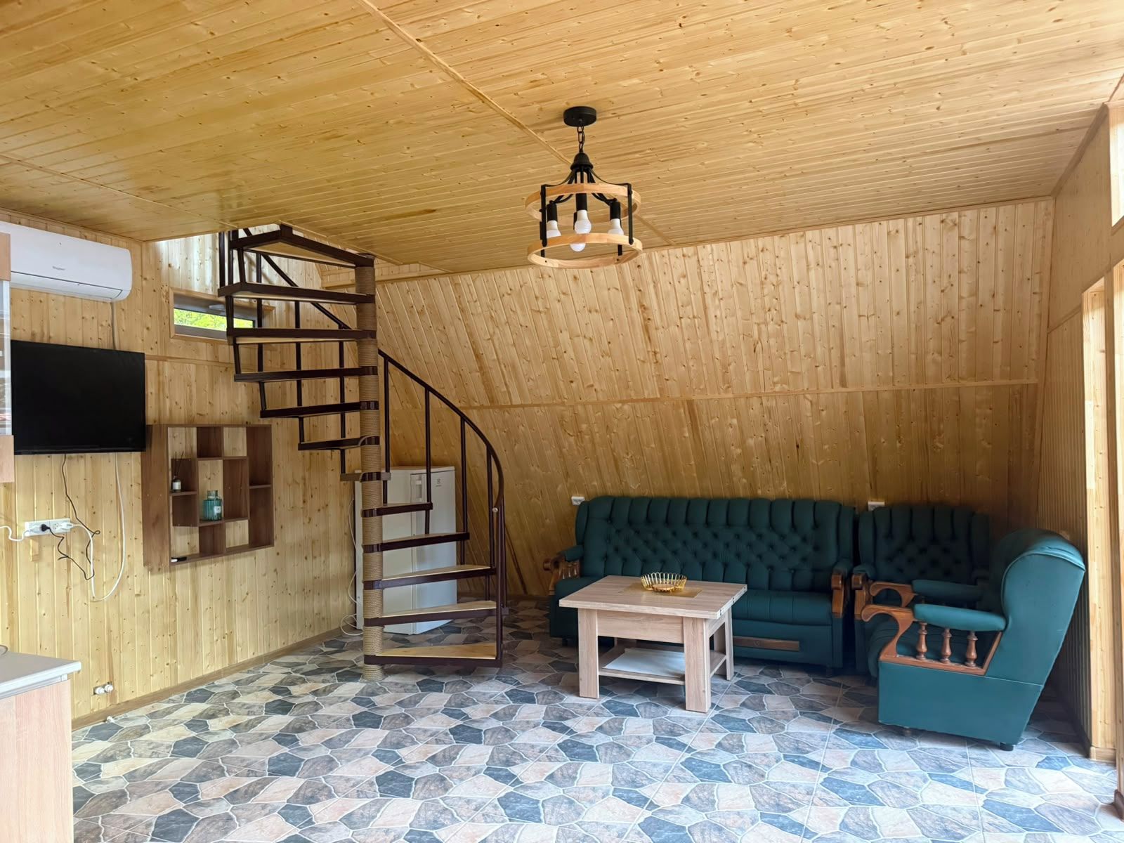 Un interior de madera con una escalera de caracol, un sofá verde, una pequeña mesa y un televisor montado en la pared.
