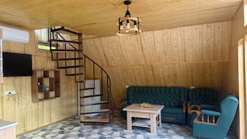 Un interior de madera con una escalera de caracol, un sofá verde, una pequeña mesa y un televisor montado en la pared.