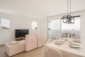 Ein modernes Wohnzimmer mit einem Flachbildfernseher, einem Sofa und einem Essbereich mit Tisch für zwei Personen.