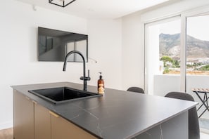 A modern kitchen with a black sink, a built-in stove, and a large window offering a view of a mountainous landscape. - Casa Limon - Amazing Townhouse in Benalmadena (Benalmádena)