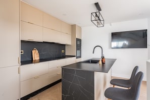 A modern kitchen with a marble countertop, integrated appliances, and a built-in island with a sink. - Casa Limon - Amazing Townhouse in Benalmadena (Benalmádena)