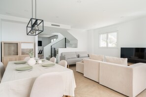 Ein großzügiger Wohnbereich mit Esstisch für vier Personen, einem grauen Sofa und einem Fernseher im Hintergrund.