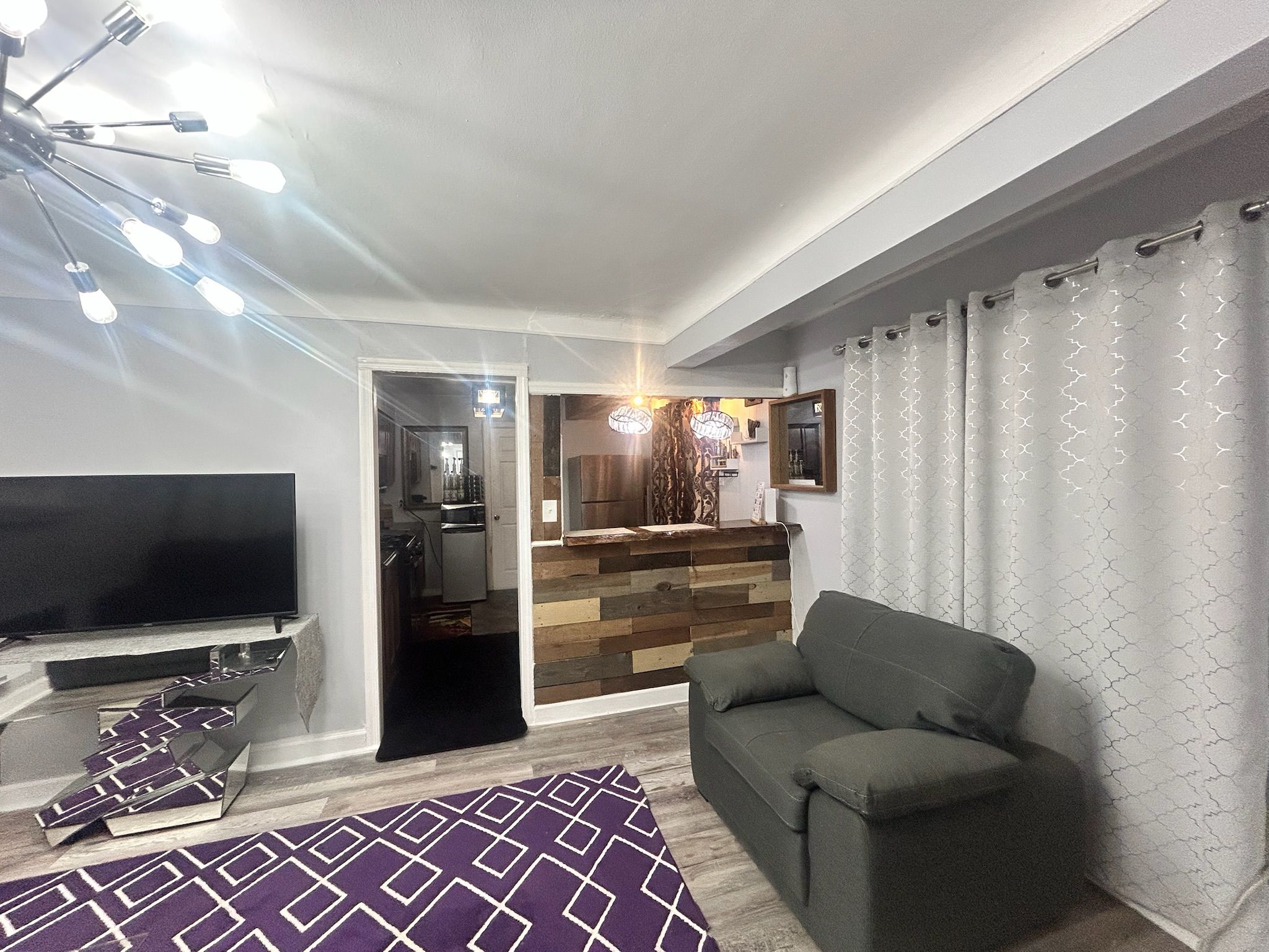 Ein modernes Wohnzimmer mit einem Flachbildfernseher, einem grauen Sofa und einem gemusterten Teppich.