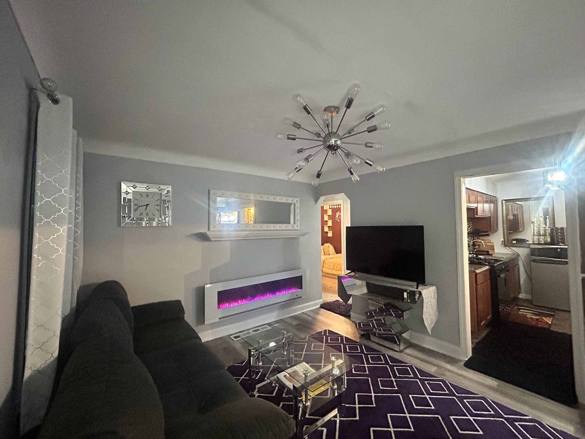 Een woonkamer met een bank, een flatscreen televisie, een open haard en een keuken, zichtbaar door een open doorgang.