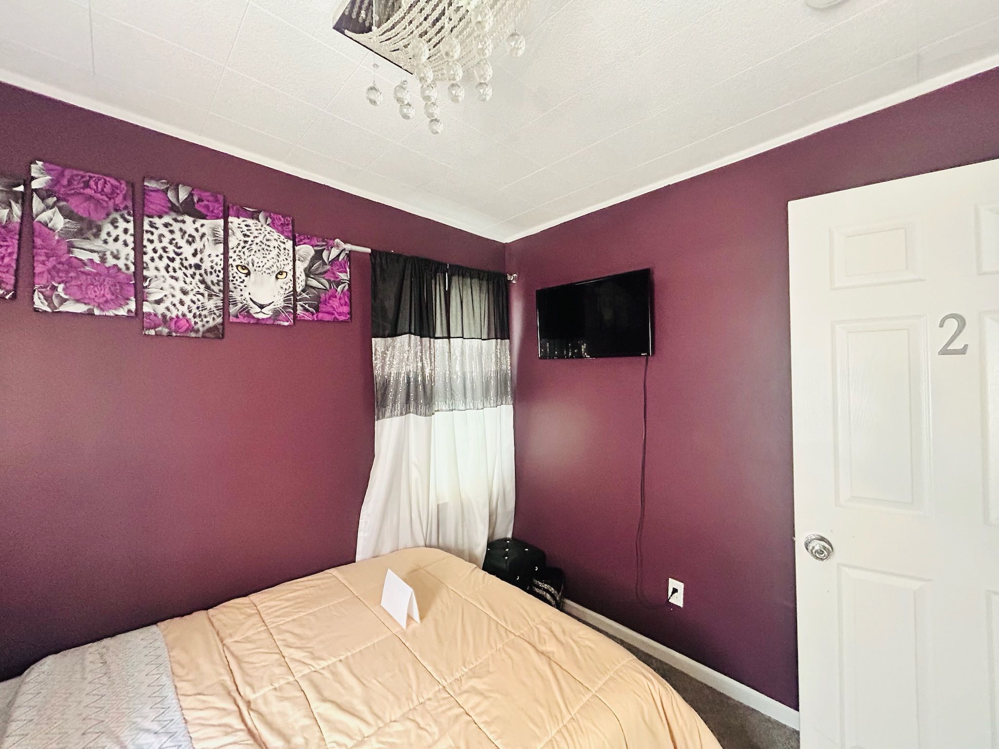 A bedroom with a bed, a television, a door with a number, and a window with curtains.