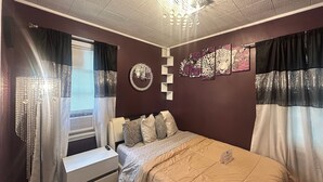 A bedroom with a bed, a bedside table, a lamp, a window with curtains, and wall art. - Charming 2-bedroom house in superb Wyandotte with AC (Wyandotte)