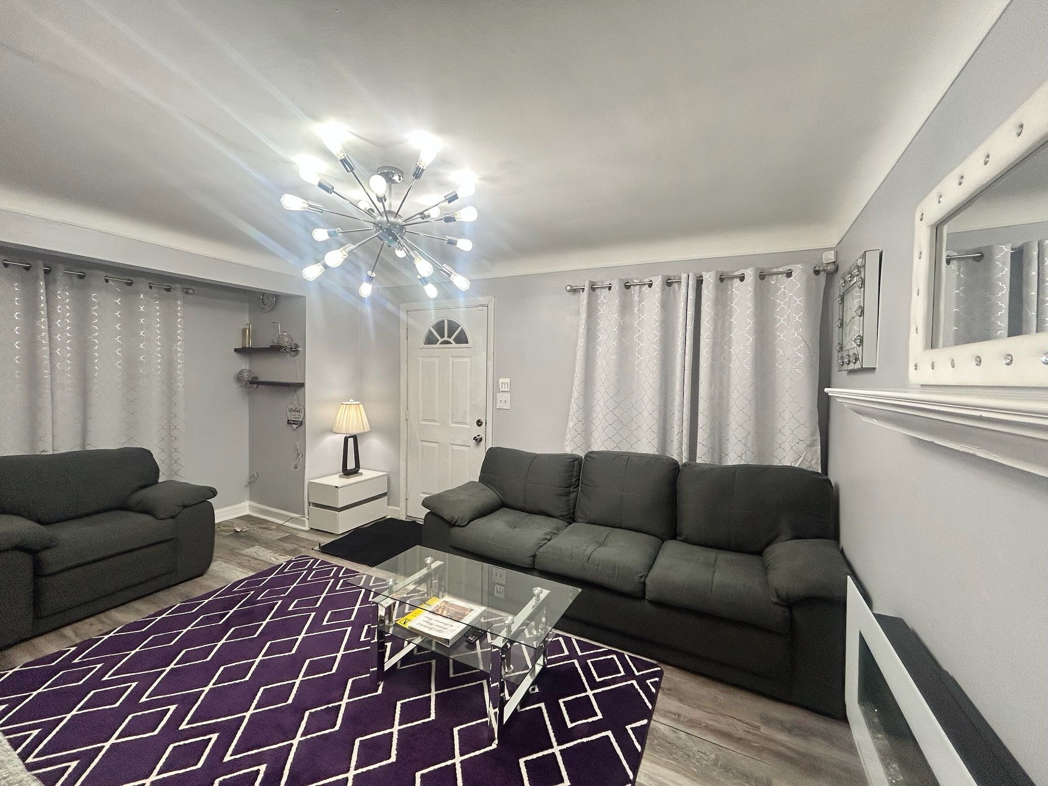 A modern living room with two sofas, a glass coffee table, and a chandelier.