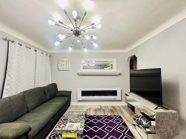 Una sala de estar con sofá, chimenea, televisor y una lámpara moderna.