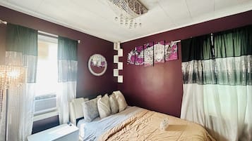 Un dormitorio con cama, ventana con cortinas, aire acondicionado de pared y decoración en la pared.