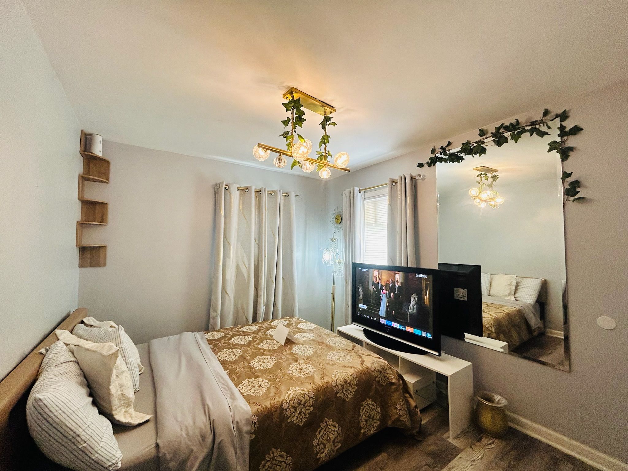 Ein Schlafzimmer mit einem Bett, einem Fernseher, einem Spiegel und einer Deckenleuchte.