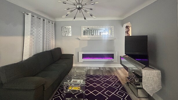 Ein modernes Wohnzimmer mit einer Couch, einem Flachbildfernseher, einem Kamin und einer dekorativen Deckenleuchte.