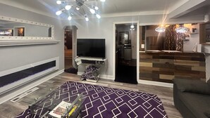 A modern living room with a flat-screen TV, a patterned rug, and a ceiling light fixture. - Charming 2-bedroom house in superb Wyandotte with AC (Wyandotte)