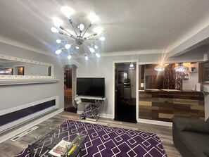 Uma sala de estar moderna com televisão de tela plana, tapete estampado e luminária no teto.