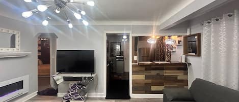 Una sala de estar con televisor, sofá, alfombra estampada y una lámpara moderna en el techo.