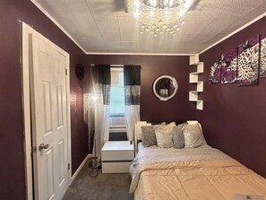 Quarto com cama, porta, espelho e lustre.