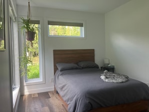 A bedroom with a bed, a nightstand, a hanging plant, and a window. - Chalet with 2 bedrooms, 5 minutes from Mount Adstock. Skiing, golf, hiking (Adstock)