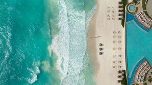 Vista aérea de um resort à beira-mar com piscina, espreguiçadeiras e uma praia de areia.