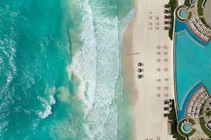 Vista aerea di un resort con piscina, lettini e spiaggia sabbiosa.