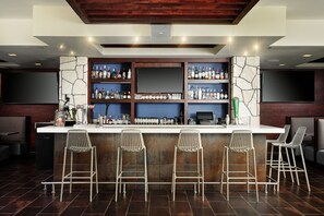 Eine Bar mit einer Wand aus Stein, mehreren Flaschenregalen und vier Metall-Barhocker.