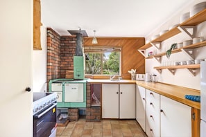 A compact kitchen with a brick wall, a vintage stove, and wooden shelves. - Parapara Lookout Coastal Stay (Takaka)
