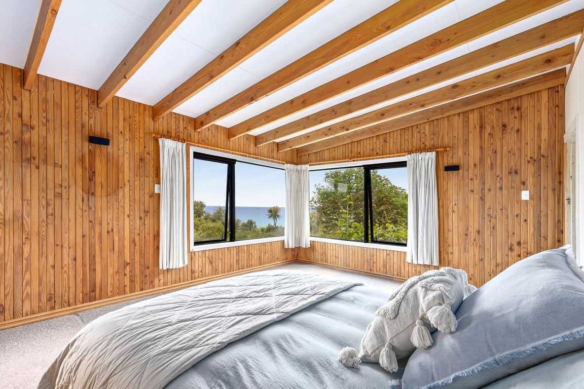 A bedroom with wooden walls, a large bed, and two windows with curtains.