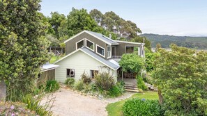 A two-story house with a sloped roof, surrounded by lush greenery and trees. - Parapara Lookout Coastal Stay (Takaka)