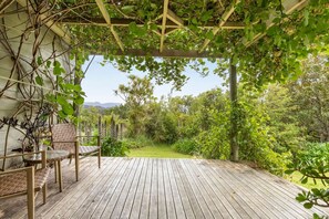 A wooden deck with a pergola covered in greenery, overlooking a lush garden. - Parapara Lookout Coastal Stay (Takaka)