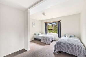 A bedroom with two single beds, a window with curtains, and a ceiling light. - Parapara Lookout Coastal Stay (Takaka)
