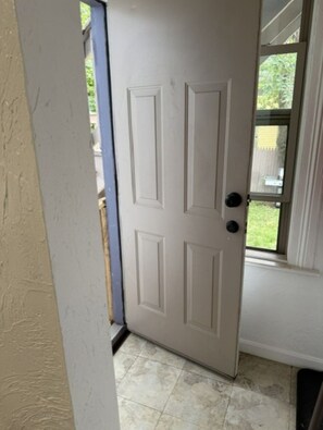 Puerta cerrada con un panel de vidrio, piso de baldosas y vista a un patio trasero a través del cristal.