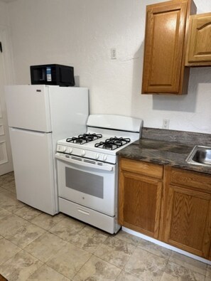 Una cocina compacta con un refrigerador, estufa y horno blancos, gabinetes de madera y una encimera de granito.