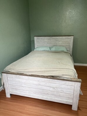 Un lit simple avec une tête de lit en bois, dans une pièce aux murs verts et au plancher en bois.