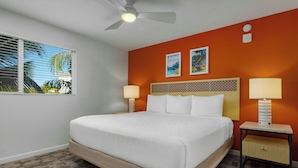 Une chambre d’hôtel avec un lit, deux tables de chevet, un ventilateur de plafond et une fenêtre avec des stores.